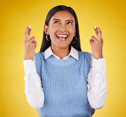 Image showing Hope, fingers crossed and young woman in a studio wishing for success, winning or achievement. Happiness, smile and excited Indian female model with a faith hand gesture isolated by yellow background