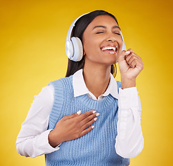 Image showing Headphones, happy and woman singing in studio while listening to music, playlist or album. Happiness, smile and Indian female model doing karaoke while streaming a song isolated by yellow background.