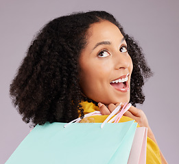 Image showing Woman, face and smile with shopping bags for discount, sale or fashion against a gray studio background. Surprised female shopper smiling and holding gifts or shop accessories posing in happiness