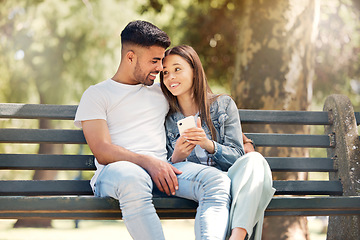 Image showing Happy couple, phone and relaxing on park bench together browsing social media and bonding in nature. Man and woman smile in happiness for relationship on mobile smartphone in the summer outdoors