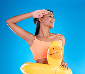 Image showing Rubber duck, smile and salute with a swimmer woman in studio on blue background wearing goggles on her head. Happy, hand gesture and swimming with an attractive young female excited to swim in summer