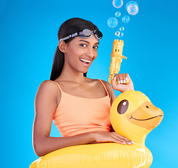 Image showing Portrait, bubbles and rubber duck with a woman on a blue background in studio ready for summer swimming. Happy, vacation and goggles with an attractive young female looking excited to relax or swim