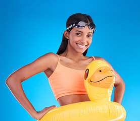 Image showing Portrait, goggles and rubber duck with a woman on a blue background in studio ready for summer swimming. Happy, vacation or hands on hips with an attractive young female looking excited for a swim