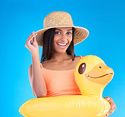 Image showing Portrait, hat and rubber duck with a woman on a blue background in studio ready for summer swimming. Happy, travel and vacation with an attractive young female looking excited to relax or swim