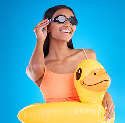 Image showing Goggles, smile and rubber duck with a woman on a blue background in studio ready for summer swimming. Happy, travel and vacation with an attractive young female looking excited to relax or swim