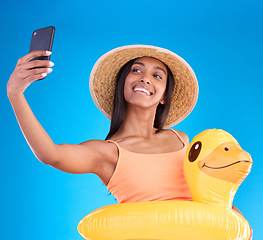 Image showing Happy woman, portrait smile and selfie on swimming vacation for profile picture with inflatable duck against a blue studio background. Excited female smiling in swimwear for photo, travel or trip