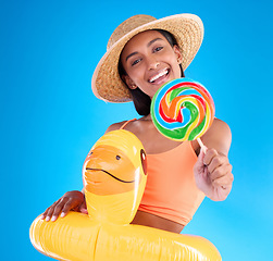 Image showing Portrait, lollipop and inflatable duck with a woman on a blue background in studio ready for summer swimming. Happy, travel and vacation with an attractive young female looking excited to relax