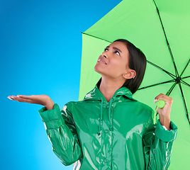 Image showing Sad, looking and a woman with an umbrella for the rain isolated on a blue background in a studio. Confused, insurance and a girl waiting for bad weather, disappointed and feeling for water in winter