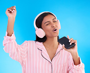 Image showing Singing, music and a woman in pyjamas with headphones isolated on a blue background in a studio. Happy, playful and a girl listening to the radio, audio or streaming songs before bedtime on a mobile