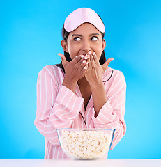 Image showing Popcorn, pajamas and thinking with a woman on a blue background in studio watching a movie for entertainment. Idea, video and night with an attractive young female eating a snack while streaming