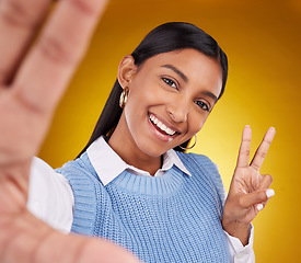 Image showing Selfie, peace sign and portrait of Indian woman in studio for happiness, confident and smile on yellow background. Emoji mockup, fashion and girl with hand gesture with beauty, cosmetics and style