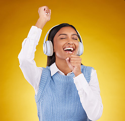 Image showing Headphones, energy and female singing in studio while listening to music, playlist or album. Happy, smile and Indian woman model doing karaoke while streaming a song isolated by yellow background.