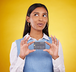 Image showing Credit card, thinking and Indian woman on yellow background for bank, investment and payment in studio. Banking mockup, finance and happy girl with plastic for budget, commerce and discount purchase