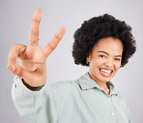 Image showing Portrait, peace sign and hand with a woman in studio on a gray background feeling happy or carefree. Smile, emoji and gesture with a happy young female indoor for freedom, wellness or good vibes