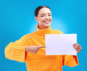 Image showing Poster, point and portrait of woman on blue background for announcement, news and information. Advertising, mockup studio and isolated happy girl with paper sign for brand, logo and product placement