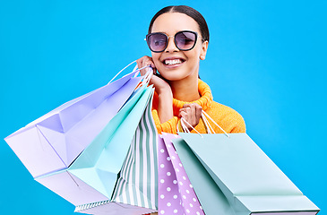 Image showing Retail bags, studio and woman portrait with a smile and happiness from boutique sale. Happy, shopping and female model with store bag and sales choice in isolated blue background with sunglasses