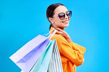 Image showing Shopping bags deal, studio and woman portrait with a smile and happiness from boutique sale. Happy, customer and female model with store bag and sales in isolated blue background with sunglasses