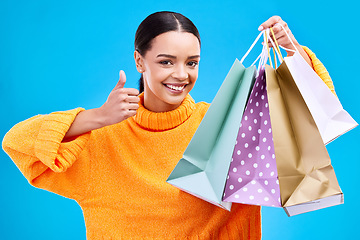 Image showing Happy woman, shopping bags and thumbs up for purchase, sale or discount against a blue studio background. Portrait of female shopper holding gift bag showing thumb emoji, yes sign or like for items