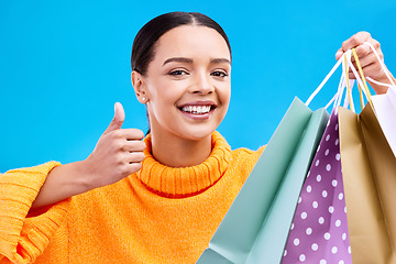 Image showing Happy woman, face and shopping bags with thumbs up for purchase, sale or discount against a blue studio background. Portrait of female shopper holding gift bag showing thumb emoji, yes sign or like