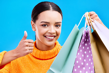 Image showing Happy woman, portrait smile and shopping bags with thumbs up for purchase, sale or discount against blue studio background. Face of female shopper with gift bag showing thumb emoji, yes sign or like