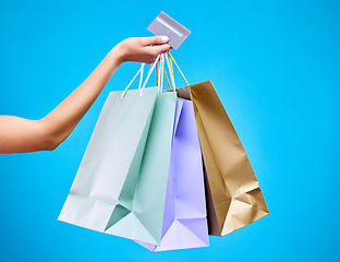 Image showing Woman, hands and shopping bags with credit card for purchase, sale or discount against a blue studio background. Hand of female shopper holding gift bag or presents for banking transaction or buying