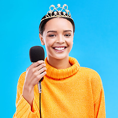 Image showing Woman, crown and microphone in studio portrait with smile for singing, recording or performance by blue background. Happy singer, girl and model with mic for speech, announcement or talk with tiara