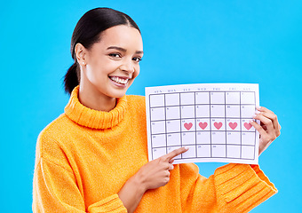 Image showing Happy, portrait and woman with a calendar in a studio to track her menstrual or ovulation cycle. Happy, smile and face of a female model pointing to a paper period chart isolated by a blue background