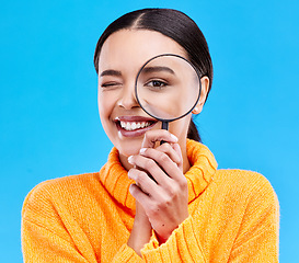 Image showing Happy, portrait and woman with a magnifier in a studio for an investigation or detective cosplay. Happiness, smile and headshot of a female model with a magnifying glass isolated by a blue background