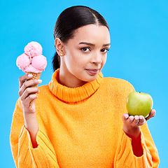 Image showing Woman, ice cream and apple with choice in portrait for health, wellness and diet by blue background. Girl, model and decision for healthy fruits, junk food and balance in nutrition for body benefits