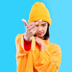 Image showing Portrait, hand gesture and rude with a woman on a blue background in studio wearing a yellow beanie or outfit. Emoji, angry and insult with an attractive young female showing the middle finger