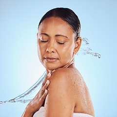 Image showing Skincare, shower and a mature woman with a water splash isolated on a blue background in a studio. Glow, anti aging and a model with hydration, liquid and fluid for skin, grooming and hygiene