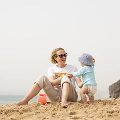 Image showing Mother playing his infant baby boy son on sandy beach enjoying summer vacationson on Lanzarote island, Spain. Family travel and vacations concept.