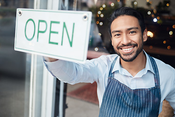 Image showing Happy Asian man, small business and smile with open sign on window for service in coffee shop or restaurant. Portrait of male entrepreneur holding billboard or poster for opening retail store or cafe