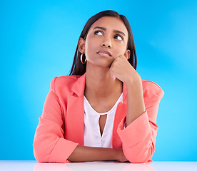 Image showing Thinking, confused and a business woman on a blue background in studio for problem solving at her desk. Idea, doubt and decision with a young female employee contemplating a thought, choice or option