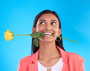 Image showing Thinking, rose and valentines day with a woman on a blue background in studio for love or romance. Idea, yellow flower and romantic with an attractive young female carrying a plant in her mouth