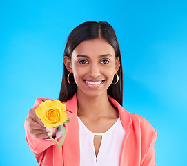 Image showing Portrait, rose and valentines day with a woman on a blue background in studio for love or romance. Face, happy and smile with an attractive young female holding a yellow flower as a romantic gift