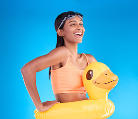 Image showing Portrait, wink and rubber duck with a woman on a blue background in studio excited for summer. Happy, smile and playful with an attractive young female ready for swimming on holiday or vacation