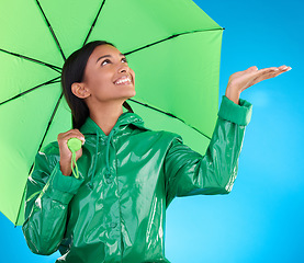 Image showing Happy, winter and a woman with an umbrella for the rain isolated on a blue background. Smile, insurance and a girl feeling for drops of water, bad weather and drizzling with shelter on a backdrop