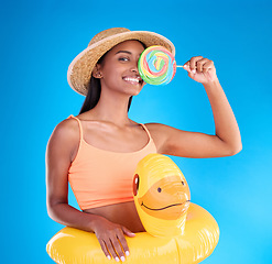 Image showing Pool float, happy woman and portrait in a studio with lollipop sweet and swimsuit with a smile. Isolated, blue background and holiday outfit of a young female with happiness and candy feeling fun