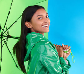 Image showing Happy, portrait and woman with an umbrella in studio with a stylish, trendy and fashion green rain coat. Life insurance, smile and Indian female model with a winter outfit isolated by blue background
