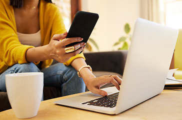 Image showing Closeup of woman working remote while typing on her laptop and holding her smartphone sitting on a sofa in a bright living room. One focused hispanic young female at home using modern technology