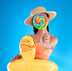 Image showing Pool float, woman and lollipop in a studio with sweet snack and swimsuit with food. Isolated, blue background and holiday outfit of a young female hiding with sweets, candy or rubber duck feeling fun