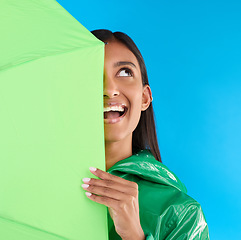 Image showing Umbrella, fun or happy woman in playful studio with raincoat, silly or happiness mockup. Goofy, face or excited female on isolated blue background or looking with smile, curious or thinking expresion