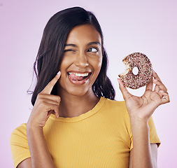 Image showing Donut, dessert and wink with woman in studio for diet, snack and happiness. Sugar, food and smile with female eating chocolate treat isolated on pink background for nutrition, playful and craving