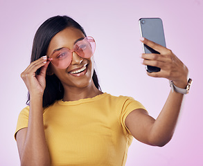 Image showing Sunglasses, selfie and happy Indian woman on pink background with cosmetics, confidence and beauty. Fashion, summer style and girl in studio take picture for social media, post and influencer blog