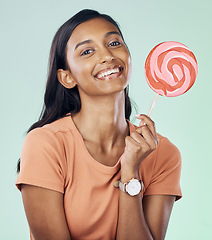 Image showing Happy, lollipop portrait and studio woman with candy, junk food or dessert product for delicious snack. Happiness, smile or Indian gen z person with sweets, sucker or sugar treats on green background