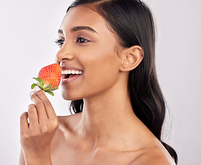 Image showing Happy, healthy and a woman eating a strawberry for nutrition isolated on a white background in a studio. Smile, thinking and an Indian girl with a fruit for a diet, breakfast or vitamins from food