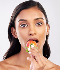 Image showing Portrait, beauty and a woman biting a strawberry in studio on a gray background for health, diet or nutrition. Face, skincare and serious with an attractive young female model eating a fruit berry