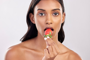 Image showing Portrait, skincare and a woman biting a strawberry in studio on a gray background for health, diet or nutrition. Face, beauty and serious with an attractive young female model eating a fruit berry