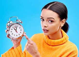 Image showing Woman, annoyed and pointing at alarm clock in portrait for warning by blue background in studio. Gen z girl, student or model with watch, time management and schedule with angry face to start morning